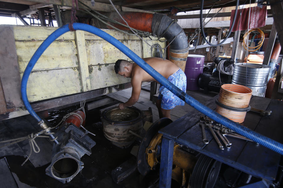 An illegal gold miner fixes a machine on a dredging barge on the Madeira river, a tributary of the Amazon river in Autazes, Amazonas state, Brazil, Thursday, Nov.25, 2021. Hundreds of mining barges have arrived during the past two weeks after rumors of gold spread, with environmentalists sounding the alarm about the unprecedented convergence of boats in the sensitive ecosystem. (AP Photo/Edmar Barros)