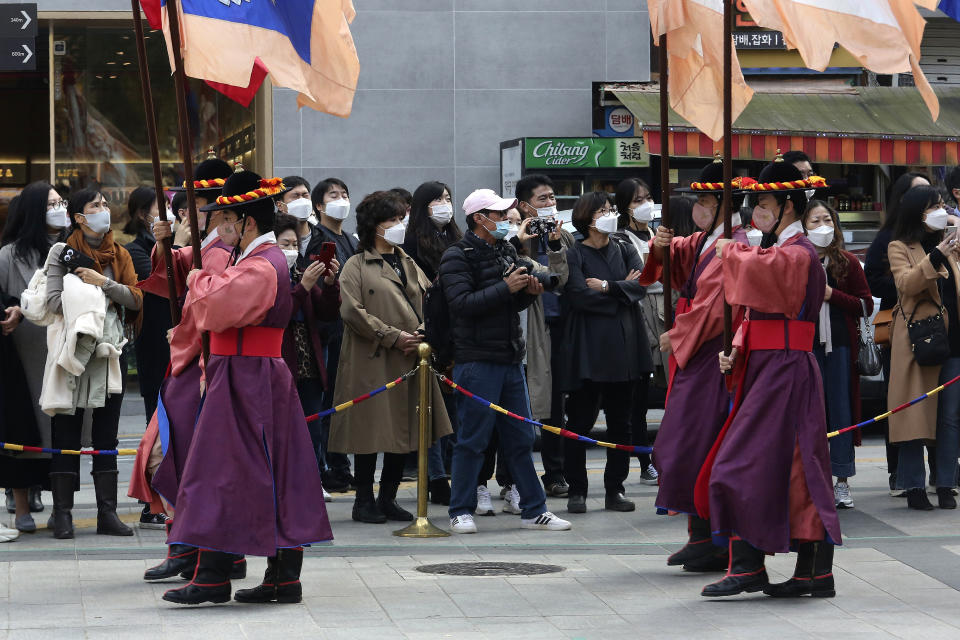 People wearing face masks watch a re-enactment ceremony of the changing of the Royal Guards, in front of the main gate of the Deoksu Palace in Seoul, South Korea, Friday, Nov. 13, 2020. South Korea has reported its biggest daily jump in COVID-19 cases in 70 days as the government began fining people who fail to wear masks in public.(AP Photo/Ahn Young-joon)