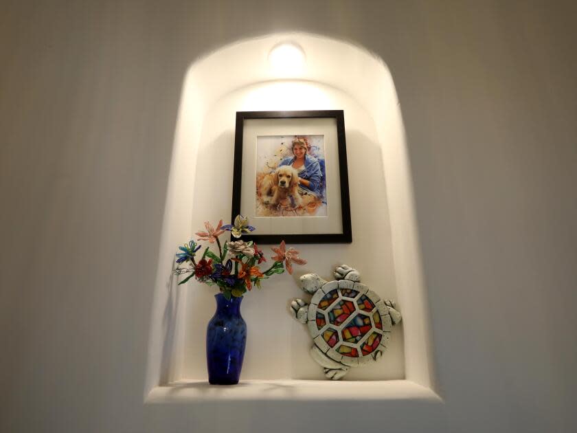 Flowers, a turtle sculpture and a picture of a woman are in a wall nook.