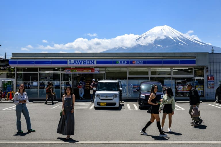 Tourists pose in front of a convenience store with Mount Fuji on May 3, 2024, before a huge black barrier which will be installed to block Mount Fuji from view (Philip FONG)