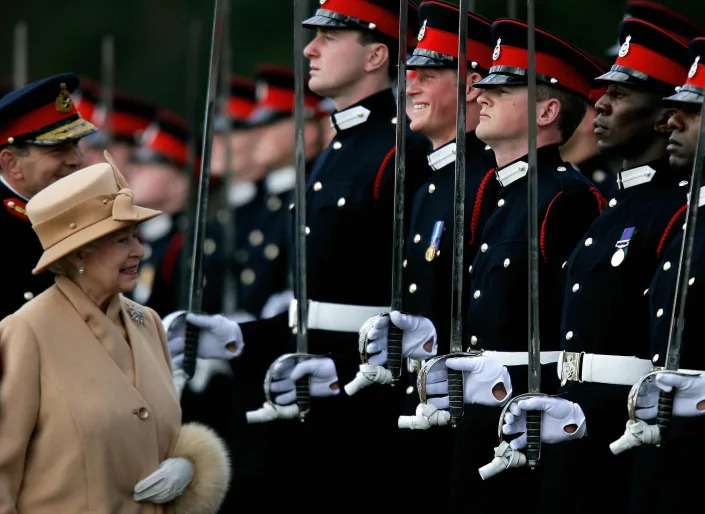 Queen Elizabeth walks by a line of soldiers, including Prince Harry, who is cracking a smile at the sight of his grandmother.