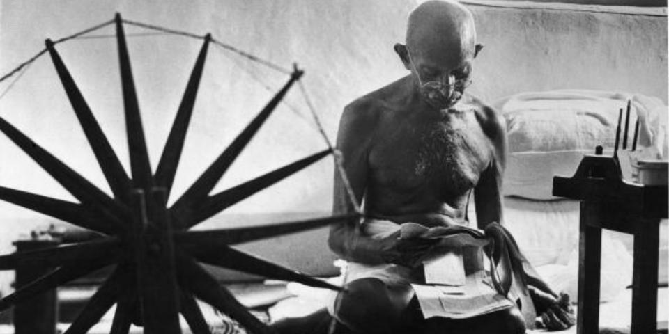 Mohandas Karamchand Gandhi reading as he sits cross-legged on floor next to a spinning wheel which looms in the foreground as a symbol of India’s struggle for Independence, at home. Photo: Margaret Bourke-White/Time & Life Pictures/Getty Images