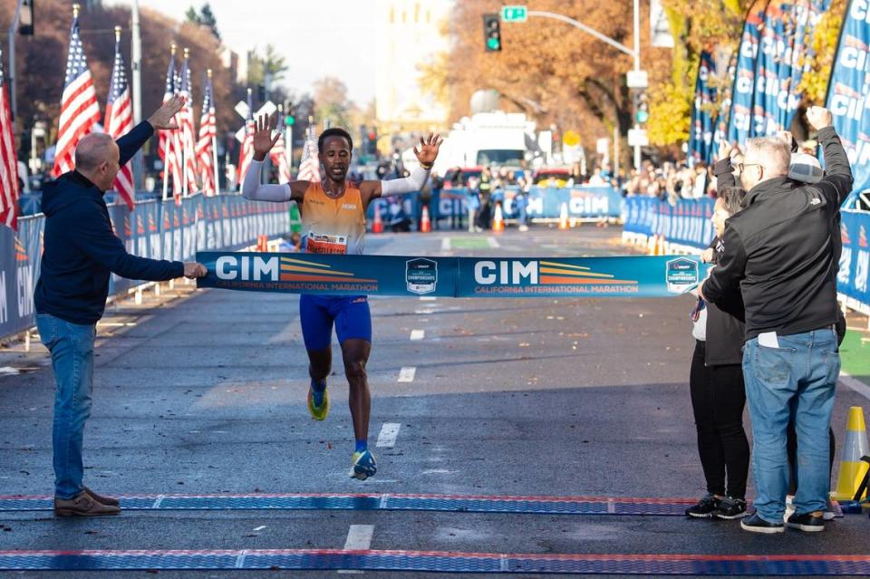 Futsum Zienasellassie crosses the finish line as Mayor Darrell Steinberg, left, holds the banner in the 2022 California International Marathon from Folsom to the state Capitol in downtown Sacramento on Sunday, Dec. 4, 2022. Zienasellassie finished first overall.