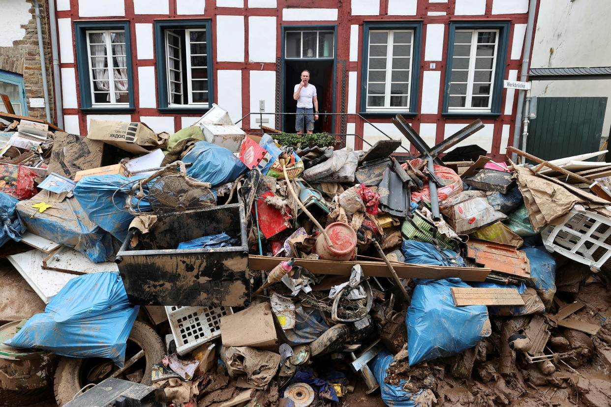 A man stands at the entrance of a home looking out at a giant mound of debris