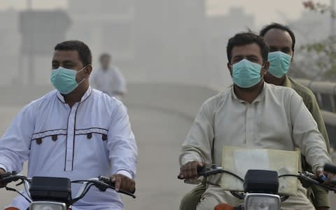 Pakistani commuters wear masks as heavy smog envelops the city in Lahore - Credit: AFP