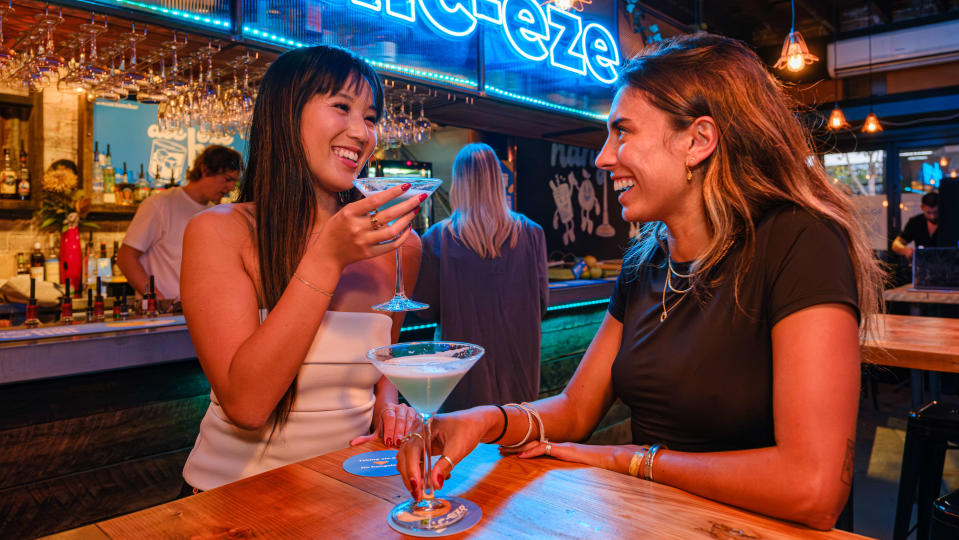 Two women sitting at a table with cocktails. 