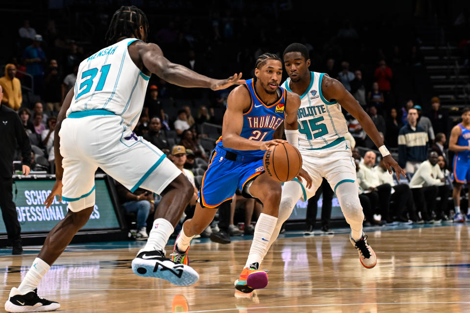 CHARLOTTE, NORTH CAROLINA – OCTOBER 15: Aaron Wiggins #21 of the Oklahoma City Thunder drives between <a class="link " href="https://sports.yahoo.com/nba/players/5865" data-i13n="sec:content-canvas;subsec:anchor_text;elm:context_link" data-ylk="slk:Edmond Sumner;sec:content-canvas;subsec:anchor_text;elm:context_link;itc:0">Edmond Sumner</a> (R) #45 of the Charlotte Hornets and <a class="link " href="https://sports.yahoo.com/nba/players/10208" data-i13n="sec:content-canvas;subsec:anchor_text;elm:context_link" data-ylk="slk:Nathan Mensah;sec:content-canvas;subsec:anchor_text;elm:context_link;itc:0">Nathan Mensah</a> #31 during the second of of the game at Spectrum Center on October 15, 2023 in Charlotte, North Carolina. (Photo by Matt Kelley/Getty Images)