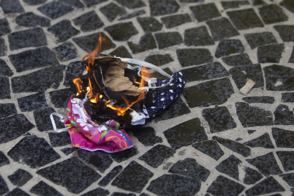 Protective masks are burned by supporters of Brazilian President Bolsonaro during a rally in favor of Bolsonaro's position that no one will be forced to use them and eventually get a coronavirus vaccine, on Copacabana beach in Rio de Janeiro, Brazil, Sunday, Nov.1, 2020. Brazil has confirmed more than 159,000 deaths from the virus, the second highest in the world, behind only the U.S. (AP Photo/Bruna Prado)