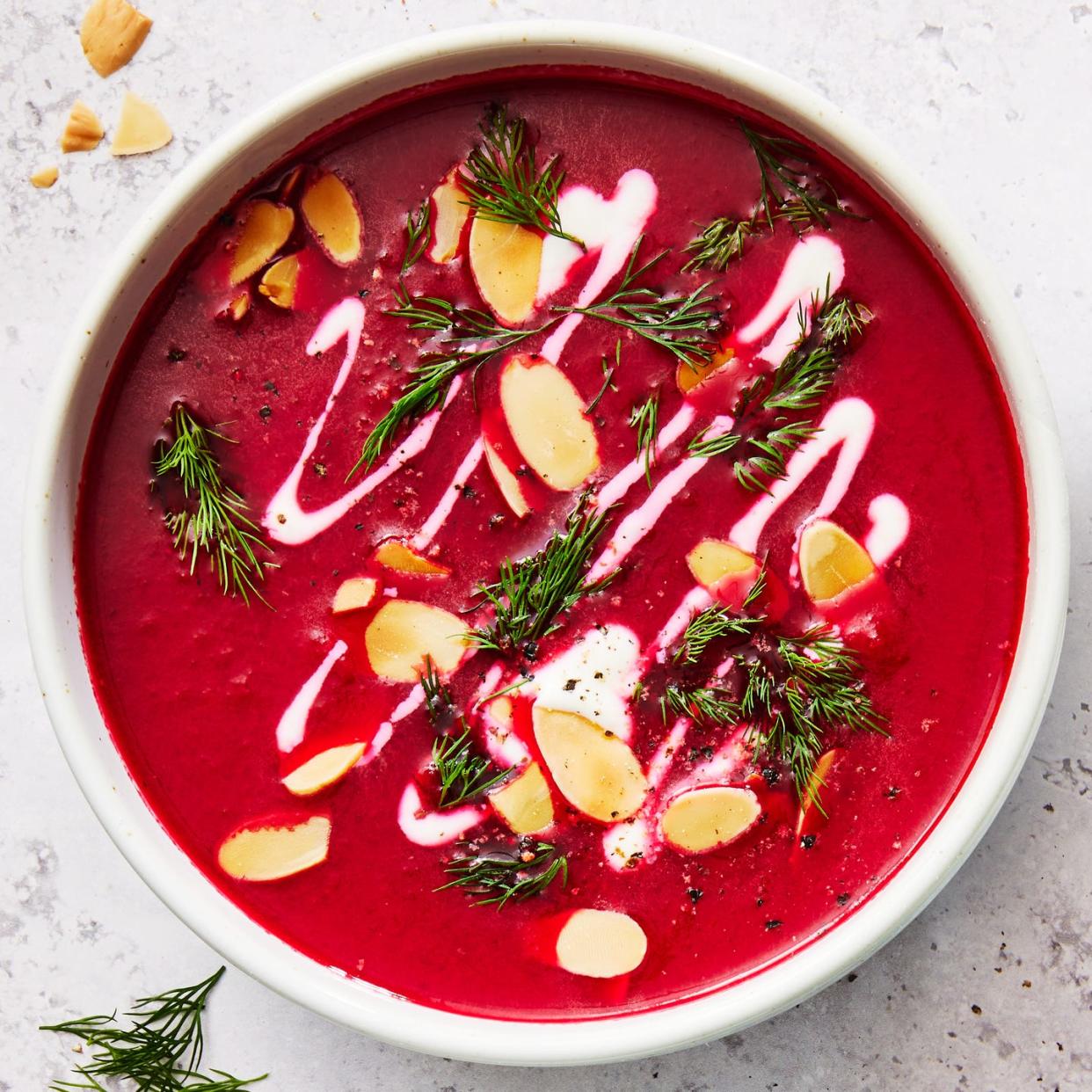 one pot harissa beet soup in a white bowl topped with almonds, herbs, and cream