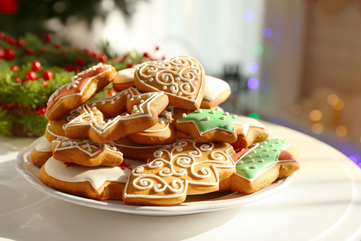 Several sugar-free Christmas cookies on a white plate on a white marble table with the blurred background of a Christmas tree and lights