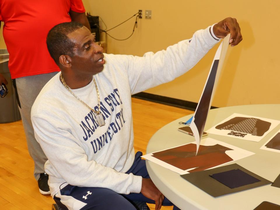 Deion Sanders analyzes design plans and fabric swatches for his team's new suits.