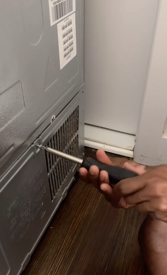 Person using a screwdriver on a vent cover at floor level