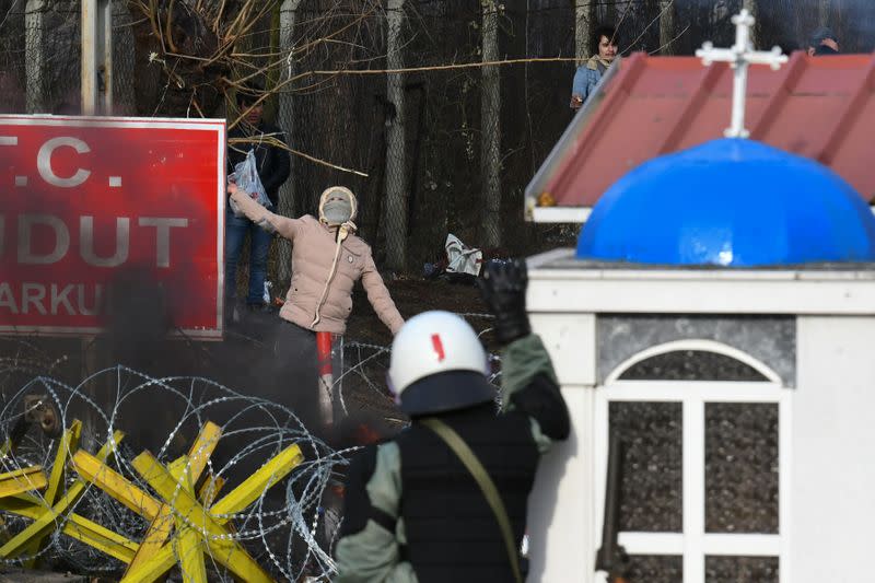 A hooded migrant who, along with other migrants wants to cross into Greece from Turkey's Pazarkule border crossing, prepares to throw a stone at a Greek riot police officer, in Kastanies