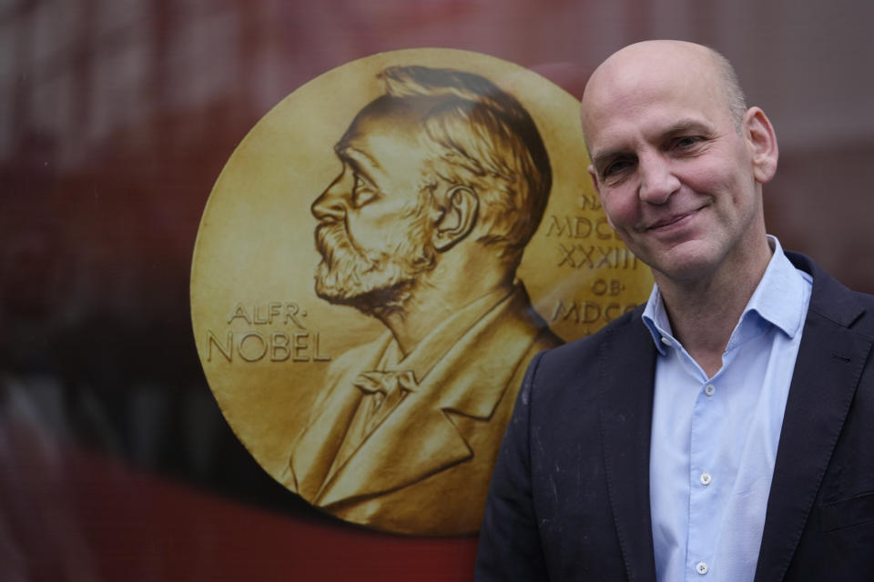 German scientist Benjamin List poses next to a poster with a medal of Alfred Nobel as arrives at the Max-Planck-Institute for Coal Research in Muelheim, Germany, Wednesday, Oct. 6, 2021. Two scientists have won the Nobel Prize for chemistry for finding an "ingenious" new way to build molecules that can be used to make everything from medicines to food flavorings. Benjamin List of Germany and Scotland-born David W.C. MacMillan developed "asymmetric organocatalysis." (AP Photo/Martin Meissner)