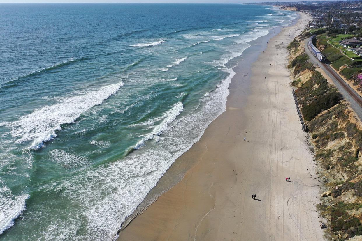 An Amtrak Pacific Surfliner train passes in front of pedestrians walking along a beach in Del Mar, California, U.S., on Thursday, May 13, 2021. Fully vaccinated Americans can do away with wearing masks, the head of the U.S. Centers for Disease Control and Prevention said, the most significant shift in federal guidelines since the start of the pandemic. Photographer: Bing Guan/Bloomberg via Getty Images