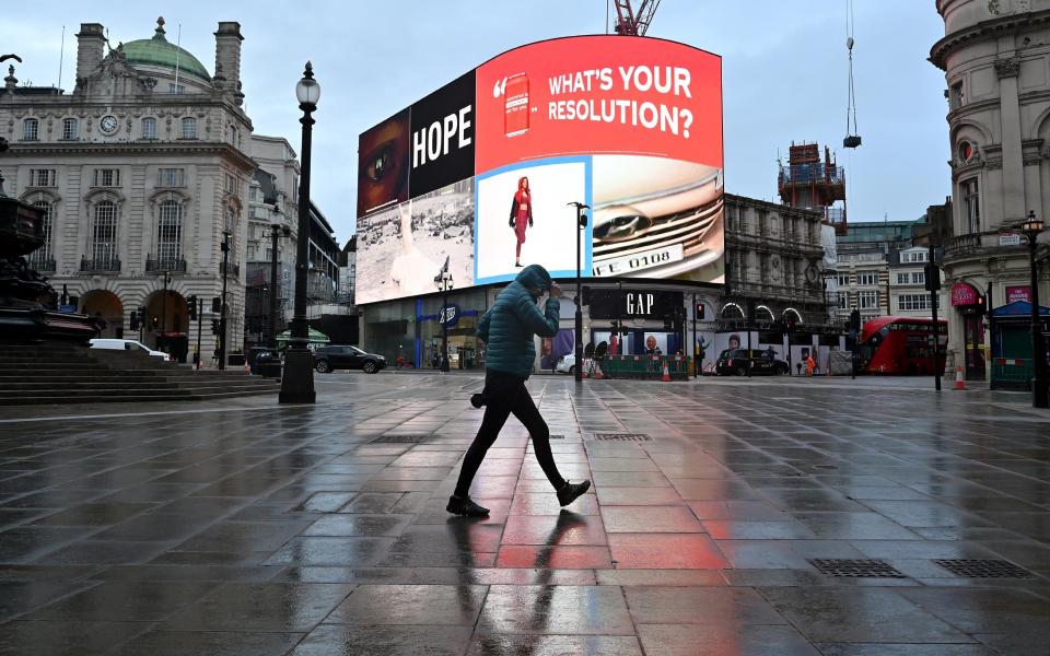 A pedestrian shelters from the rain as they walk across an almost deserted Piccadilly Circus as Britain enters a national lockdown in London on January 5, 2021 - JUSTIN TALLIS