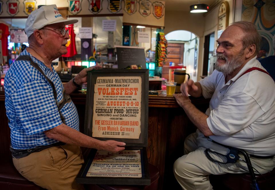 Tom Memmer III, left, and Paul Bockstege chat about the old days while showing off a Volksfest poster from 1962 at Germania Maennerchor’s Rathskeller Thursday, July 27, 2023.