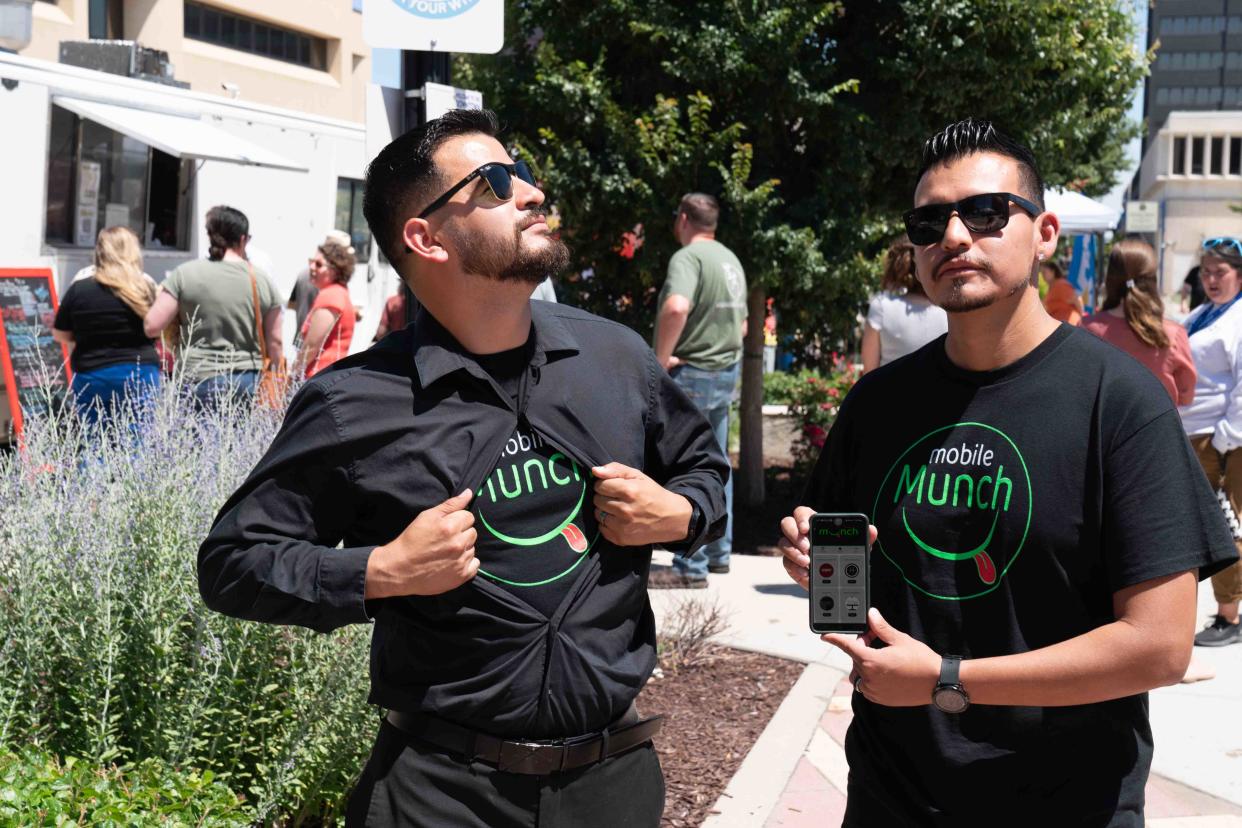 Mobile Munch founders Jorge Hernandez, left, and Rogelio Zamora Jr. show off their app in front of a busy line of food trucks outside at Evergy Plaza. The duo created the app to help find local food trucks around town.