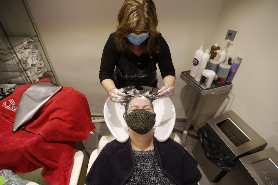 Hairdresser Andrea Roder washes the hair of a client in Budapest, Hungary, Wednesday April 7, 2021. Hungary's government lifted several lockdown restrictions on Wednesday, even as some doctors and medical experts urged caution after a record-breaking day of COVID-19 deaths, a move that came as Hungary reached 2.5 million first-dose vaccinations, a benchmark the government set for when a gradual reopening could move forward. (AP Photo/Laszlo Balogh)