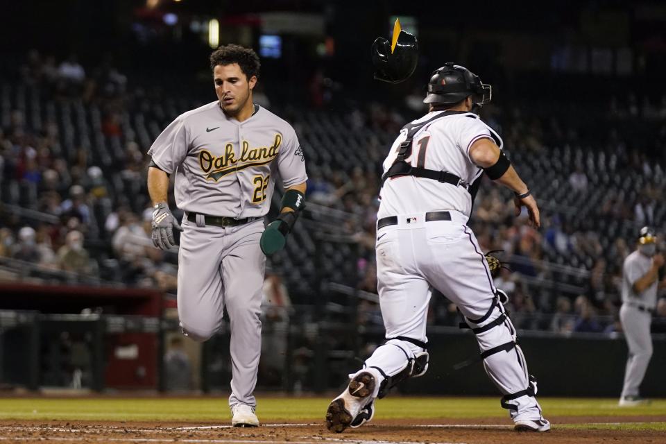 Oakland Athletics' Ramon Laureano (22) scores a run as his helmet hits Arizona Diamondbacks catcher Stephen Vogt, right, during the third inning of a baseball game Monday, April 12, 2021, in Phoenix. (AP Photo/Ross D. Franklin)