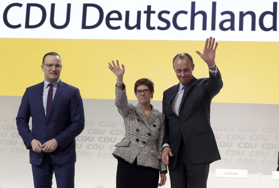 In this Friday, Dec. 7, 2018 photo then newly elected CDU chairwoman Annegret Kramp-Karrenbauer, center, is flanked by the defeated candidates Jens Spahn, left, and Friedrich Merz, right, as she waves during the party convention of the Christian Democratic Party CDU in Hamburg, Germany. Angela Merkel's designated successor will quit her role as head of the Germany's strongest party and won't stand for the chancellorship following a debacle in a regional election. (AP Photo/Michael Sohn)