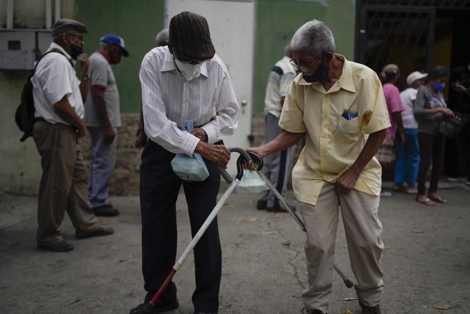 ARCHIVO - Hombres golpean sus bastones para despedirse después de recibir sus comidas donadas en un comedor de beneficencia en el barrio de La Vega de Caracas, Venezuela, el 11 de marzo de 2022. (AP Foto/Ariana Cubillos, Archivo)