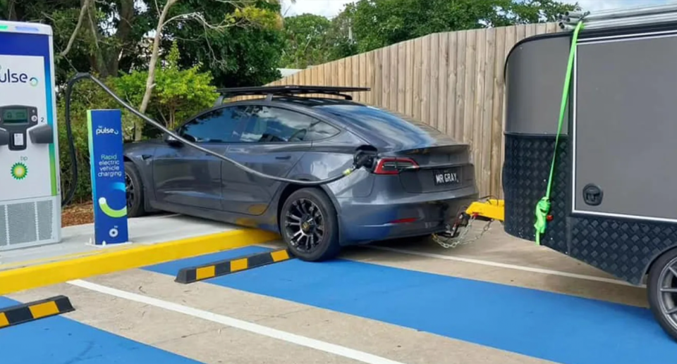 A Tesla mounted the curb to charge because a trailer towed behind the car blocked access to the short charging cable. 