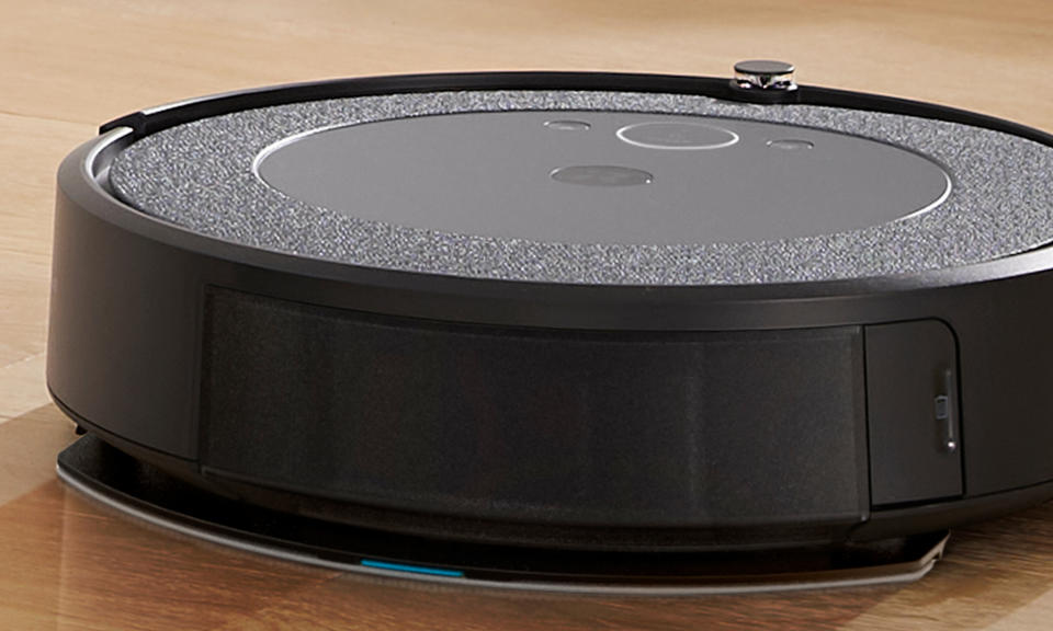 Closeup marketing photo of the iRobot i5+. The robot vacuum has a gray / black appearance and is on a hardwood floor.