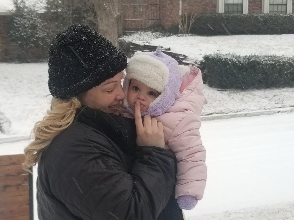 A mom, wearing a black hat and jacket, holds her baby in the snow.