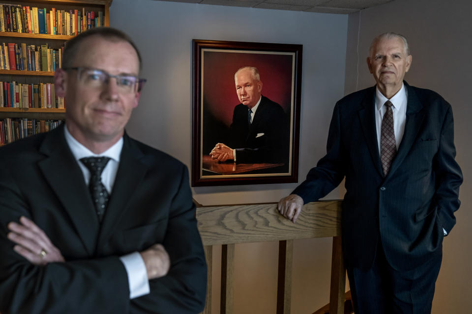 A portrait of John Birch Society founder, Robert Welch, hangs behind CEO Bill Hahn, left, and Art Thompson, a retired Society president, at the organization's headquarters in Appleton, Wis., Thursday, Nov. 17, 2022. “As Mr. Welch came out with on Day One: There is a conspiracy,” Hahn says. “It’s no different today than it was back in December 1958.” (AP Photo/David Goldman)