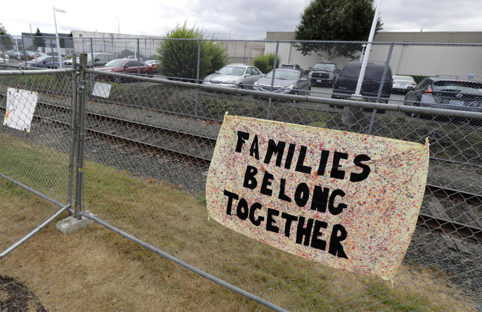 FILE - This July 10, 2018 file photo shows a sign that reads "Families Belong Together" on a fence outside the Northwest Detention Center in Tacoma, Wash. A federal judge in Seattle on Friday, June 28, 2019, is hearing a challenge to a new Trump administration policy that would keep thousands of asylum seekers locked up while they pursue their cases, instead of allowing them to be released on bond. (AP Photo/Ted S. Warren, File)