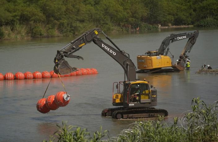 Workers on Wednesday deploy large buoys to be used as a border barrier along the banks of the Rio Grande in Eagle Pass. The floating barrier is being deployed in an effort to block migrants from entering Texas from Mexico.