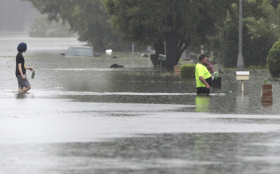 A man, right, and a woman walk across a flooded street in Windsor, north west of Sydney, Australia, Tuesday, March 23, 2021. Hundreds of people have been rescued from floodwaters that have isolated dozens of towns in Australia's most populous state New South Wales and forced thousands to evacuate their homes as record rain continues to inundate the country's east coast. (AP Photo/Rick Rycroft)