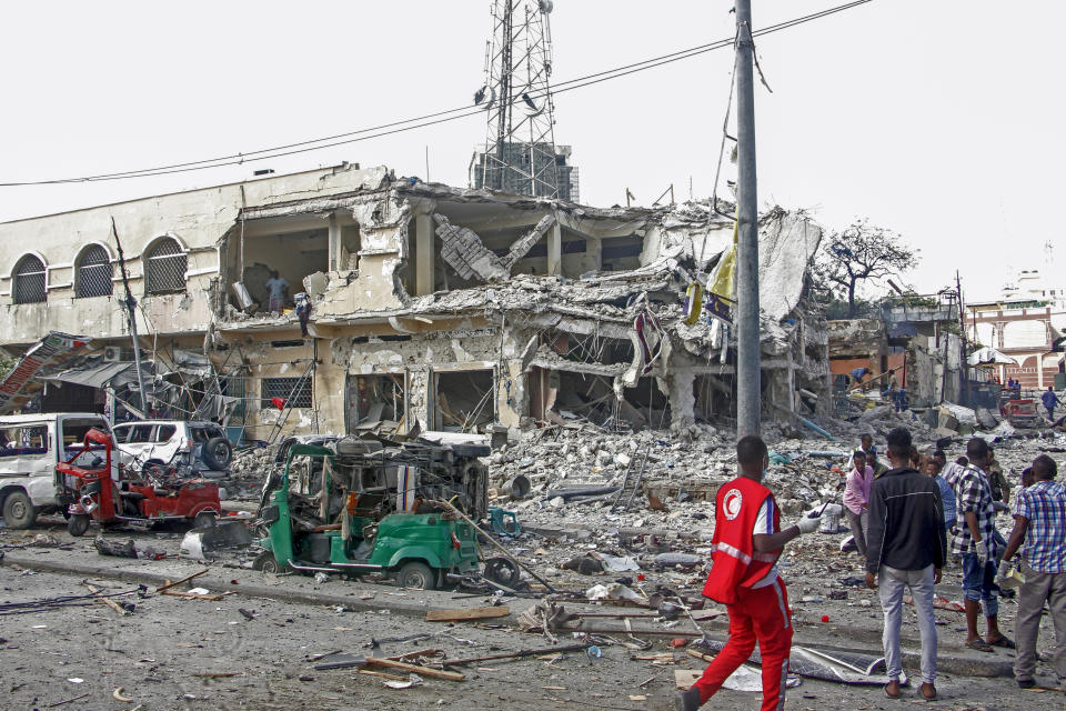 People observe a destroyed building and vehicles at the scene of a two car bombs attack in Mogadishu, Somalia, Saturday Oct. 29, 2022. Two car bombs exploded Saturday at a busy junction in Somalia's capital near key government offices, leaving "scores of civilian casualties," police told state media. (AP Photo/Farah Abdi Warsameh)