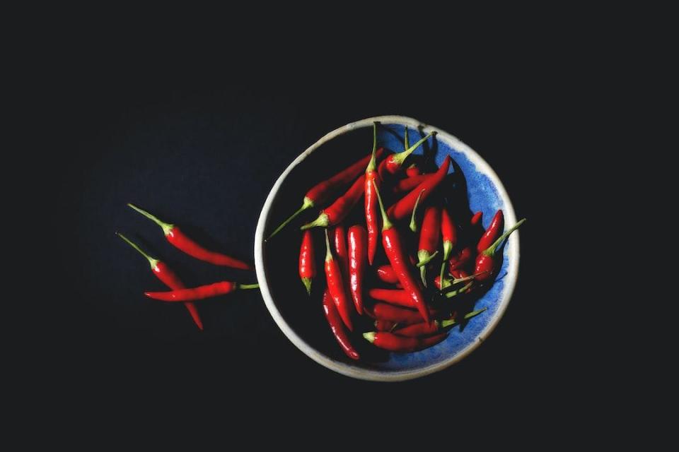 Spicy red peppers sitting in a bowl on top of a black background.