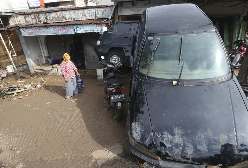 A women stands near the wreckage of cars that were swept away by flood in Bekasi, West Java, Indonesia, Friday, Jan. 3, 2020. Severe flooding in greater Jakarta has killed scores of people and displaced tens of thousands others, the country's disaster management agency said. (AP Photo/Achmad Ibrahim)