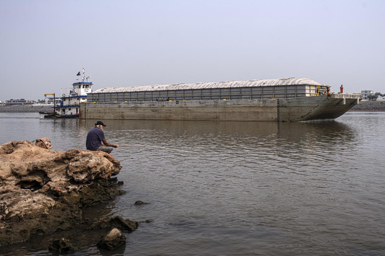 A man fishes on the shore of the Paraguay River where a tugboat pushes a barge amid low water levels and a drought in Mariano Roque Alonso, Paraguay, Monday, Sept. 9, 2024. (AP Photo/Jorge Saenz)