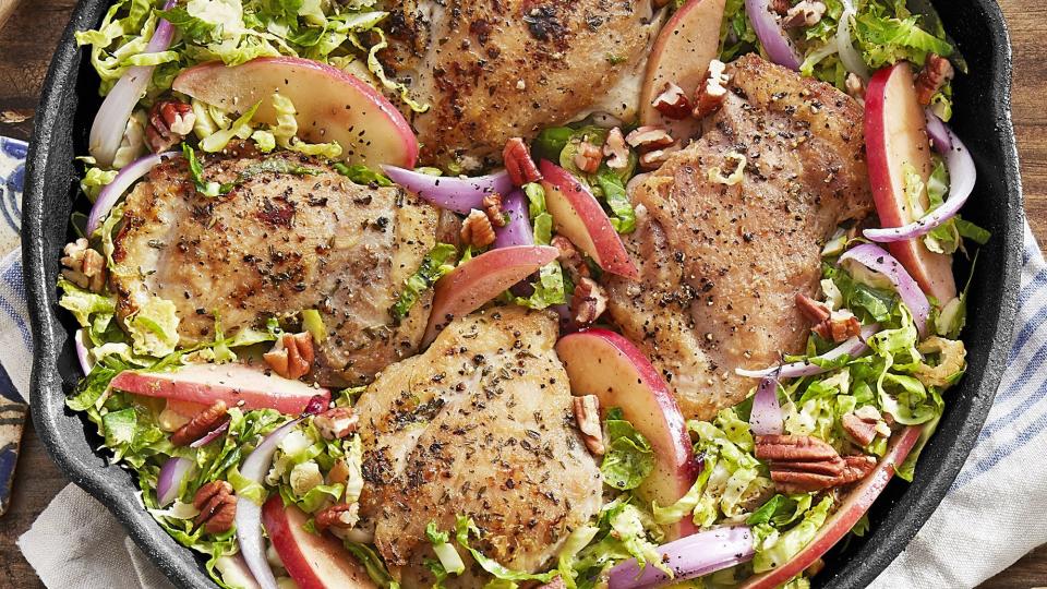 skillet chicken with brussels sprouts and apples on a kitchen towel on a wooden table