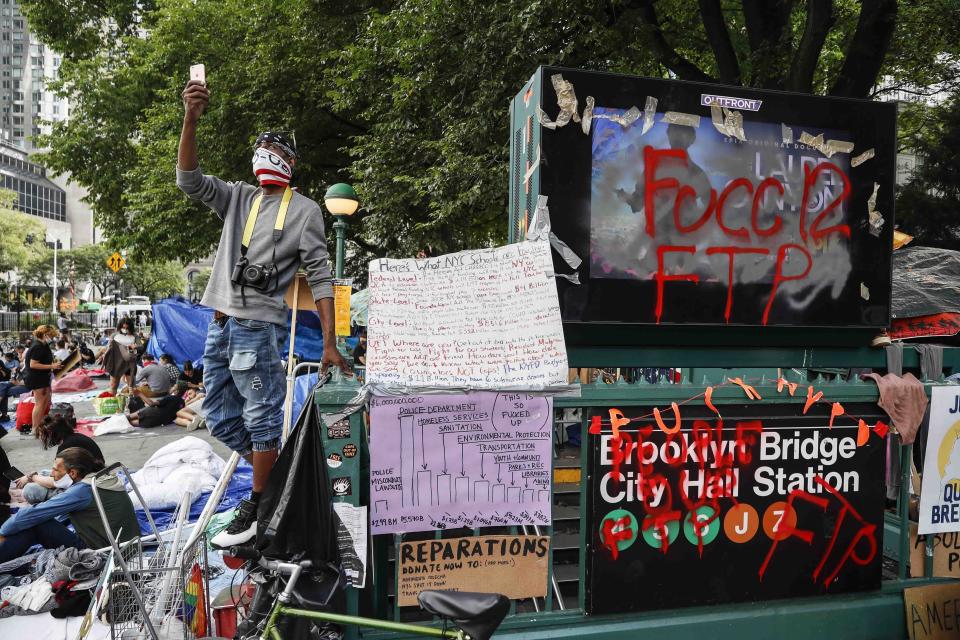 Protesters gather beside a subway station entrance at an encampment outside City Hall, Tuesday, June 30, 2020, in New York. New York City lawmakers are holding a high-stakes debate on the city budget as activists demand a $1 billion shift from policing to social services and the city grapples with multibillion-dollar losses because of the coronavirus pandemic. (AP Photo/John Minchillo)