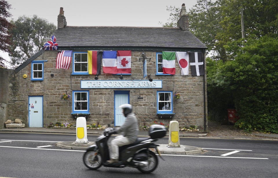 FILE - In this Wednesday, June 9, 2021 file photo, a man rides a motorbike past a pub with flags of the G7 nations and the flag of Cornwall in St. Ives, Cornwall, England. Towering steel fences and masses of police have transformed the Cornish seaside as leaders of the Group of Seven wealthy democracies descent for a summit near St. Ives in Cornwall, a popular holiday destination. A huge frigate dominates the coastline, armed soldiers guard the main sites and some 5,000 extra police officers have been deployed to the area. (AP Photo/Jon Super, File)