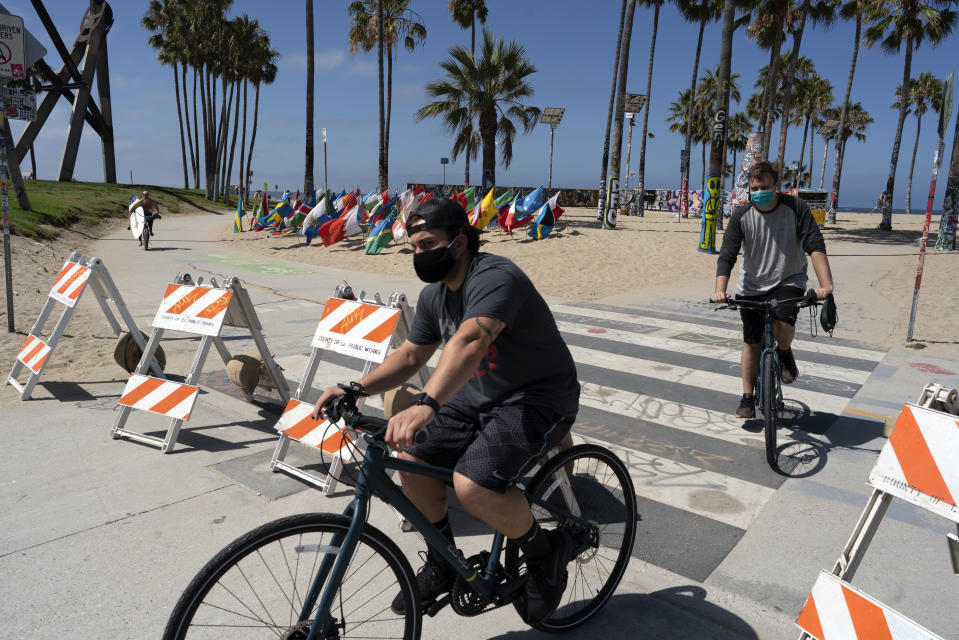 Cyclists wearing masks to protect from coronavirus cross a closed section of Venice beach on Friday, July 3, 2020 in Los Angeles. California's governor is urging people to wear masks and skip Fourth of July family gatherings as the state's coronavirus tally rises. All L.A. County beaches are closed from July 3 through July 6, to prevent dangerous crowding. Rates of COVID-19 infections and hospitalizations have soared in the past two weeks after falling last month. (AP Photo/Richard Vogel)