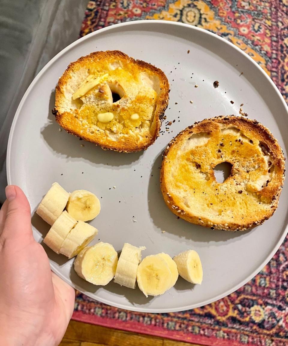 The write holding a plate with a bagel cut in half and sliced bananas