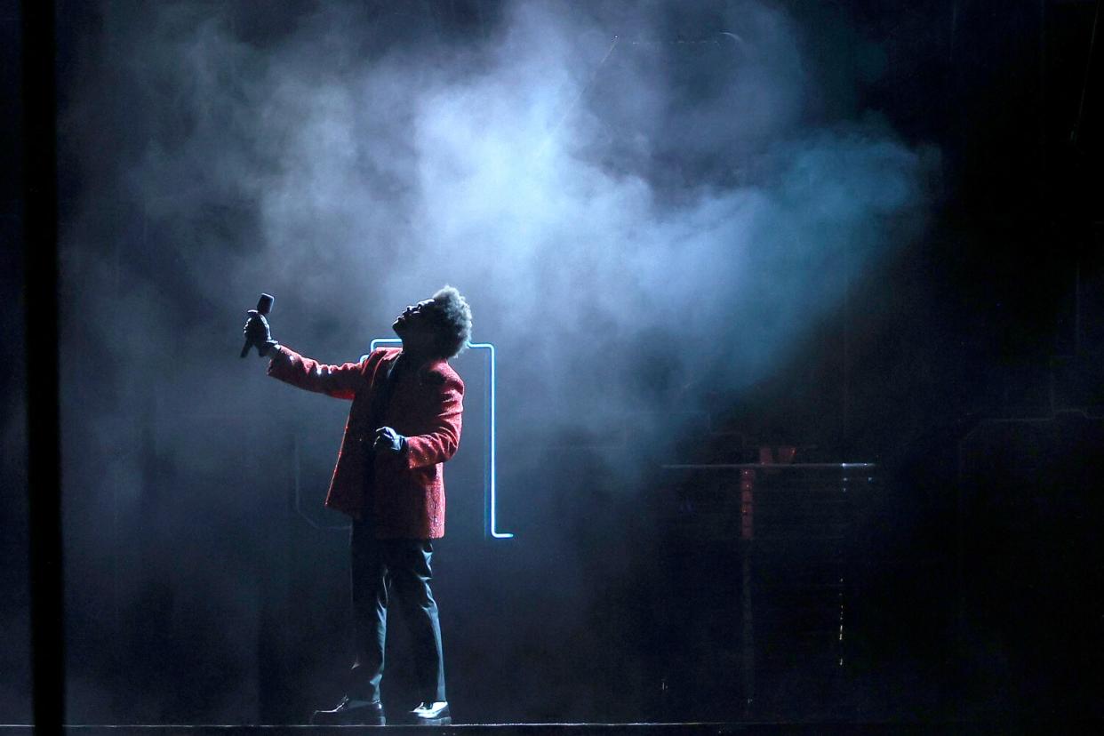 A man in a red sports jacket performs on a stage shrouded in smoke