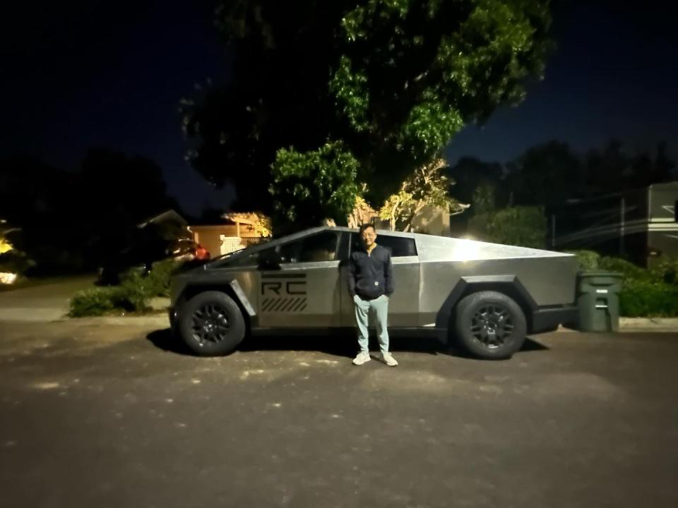 A man stands next to the Tesla Cybertruck prototype. His head is about as high as the roof, the bed walls reach as high as his armpits.