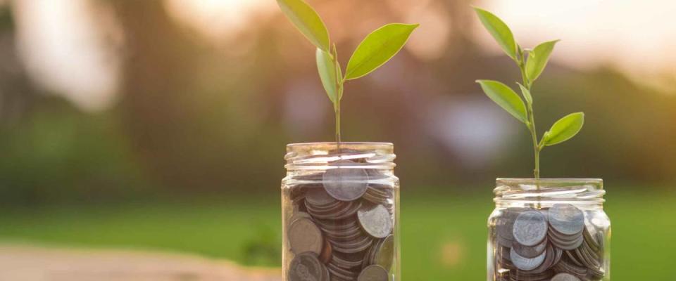 Saving money by hand puting coins in jug glass on nature background