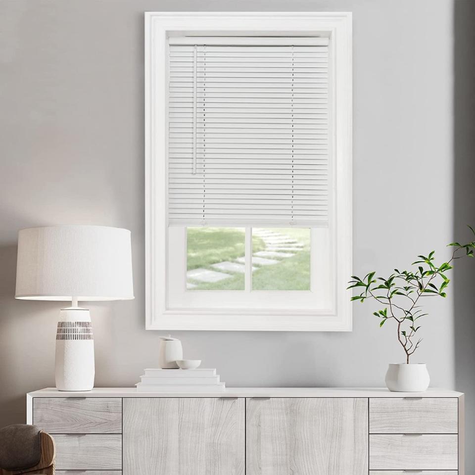 A window with partially open mini blinds over a cabinet