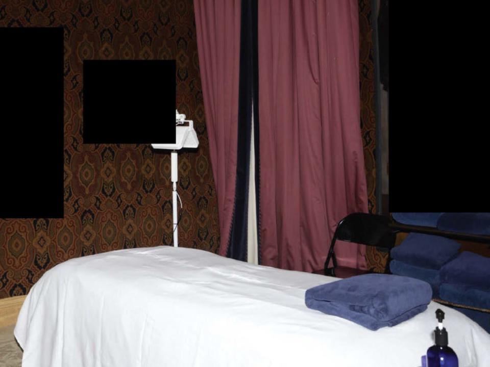 A photograph, labeled as a government exhibit, showing a massage table covered in a white cloth in a dark room