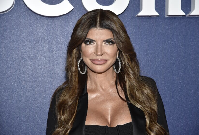 A woman with long brown hair posing in hoop earrings and a black shirt