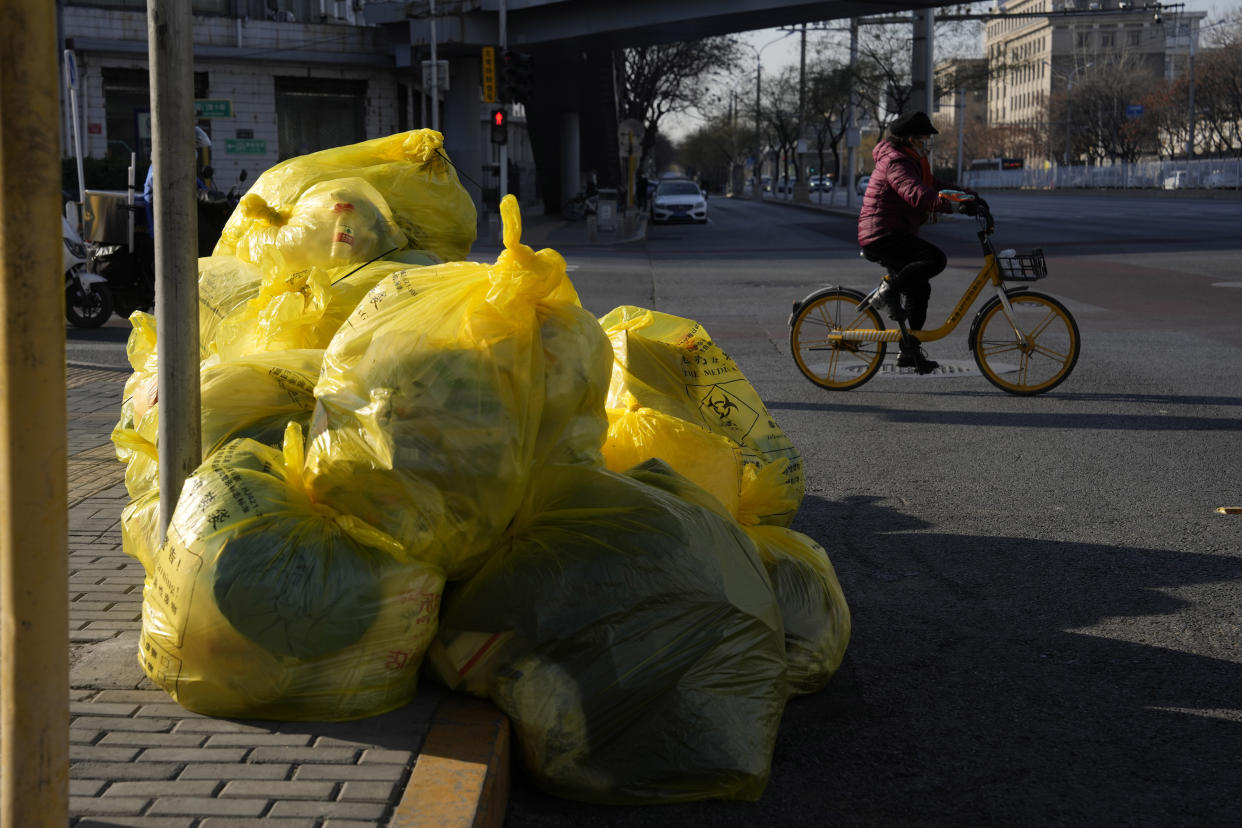 A cyclist passes by household waste inside yellow trash bags marked as medical waste in Beijing, Wednesday, Dec. 7, 2022. In a sharp reversal, China has announced a series of measures rolling back some of the most draconian anti-COVID-19 restrictions. (AP Photo/Ng Han Guan)