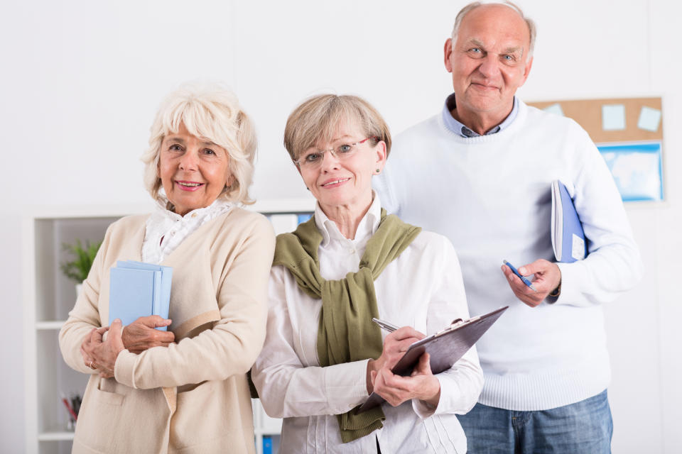 Three seniors holding notebooks and clipboards while standing together